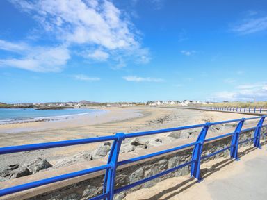 A beach with a sandy shore and a stone wall with blue railings at Corrie Knowe in Trearddur Bay