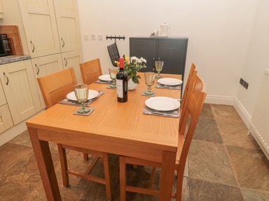 A dining table set for four with plates glasses and a bottle of wine in a kitchen at Little Tern in Seahouses