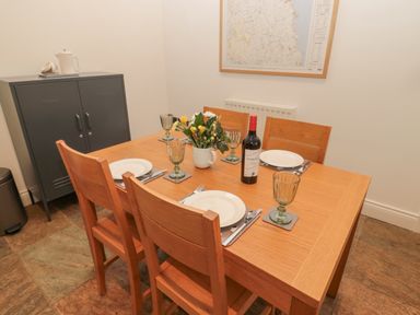 A dining table with four wooden chairs set with plates glasses and cutlery a bottle of wine and flowers in a vase on the table at Little Tern in Seahouses