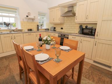 A kitchen with wooden table and chairs set for four with plates glasses and a bottle of wine at Little Tern in Seahouses