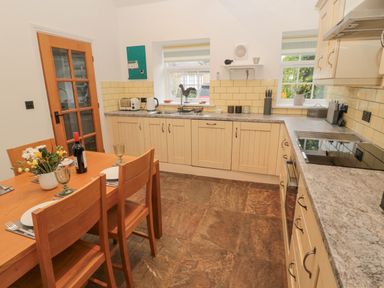 A kitchen with a wooden dining table and chairs a wine bottle a toaster kettle and cabinets at Little Tern in Seahouses