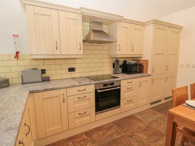 A kitchen with wooden cabinets a stovetop oven microwave and dining table at Little Tern in Seahouses