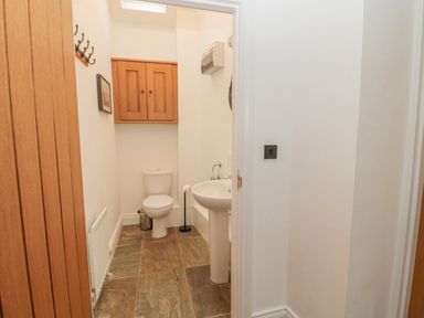 A small bathroom with a toilet a sink a wooden cabinet and a tiled floor at Little Tern in Seahouses