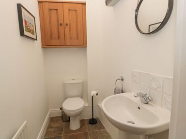 A small bathroom with a toilet sink wooden cabinet mirror and framed picture at Little Tern in Seahouses