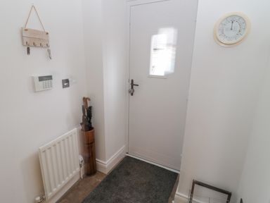 An entryway with a white door a radiator umbrella stand a key holder and a wall clock at Little Tern in Seahouses