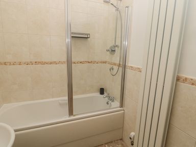A bathroom with a bathtub and shower with sliding glass doors and tiled walls at Little Tern in Seahouses