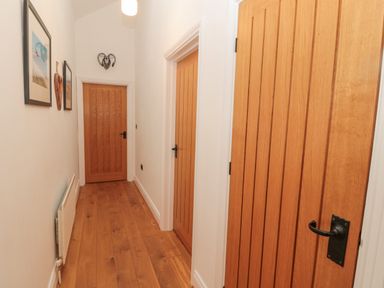 A hallway with three wooden doors wooden floor and framed pictures on the wall at Little Tern in Seahouses