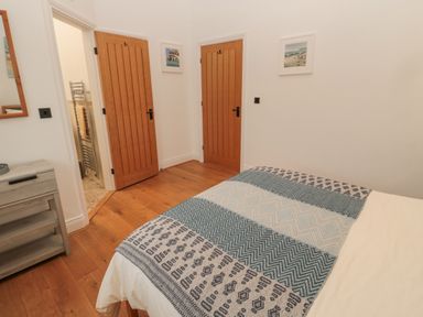 A bedroom with a bed covered by a patterned throw two wooden doors and a small grey wooden cabinet at Little Tern in Seahouses