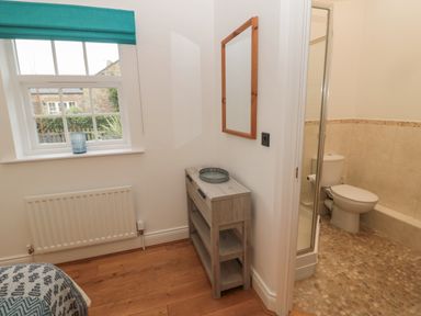 A corner of a bedroom with a window and a wooden shelf next to a bathroom with a toilet at Little Tern in Seahouses