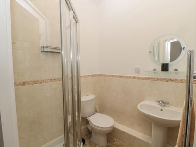 A bathroom with a shower enclosure toilet sink and round mirror at Little Tern in Seahouses