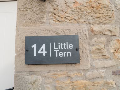 A black house number sign with number 14 and name Little Tern on a stone wall at Little Tern in Seahouses