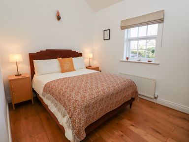 A bedroom with a double bed bedside tables and lamps a window and wooden flooring at Little Tern in Seahouses