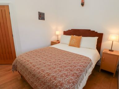 A bedroom with a double bed two bedside tables with lamps and a wooden door at Little Tern in Seahouses