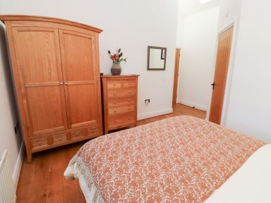 A bedroom with wooden wardrobe chest of drawers and bed covered with patterned orange blanket at Little Tern in Seahouses