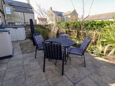 An outdoor patio with a round metal table and four metal chairs with striped cushions at Little Tern in Seahouses