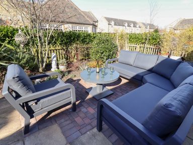 An outdoor seating area with blue cushioned chairs and a round table with glasses and a bottle at Little Tern in Seahouses