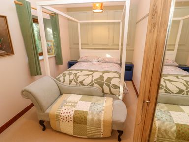 A bedroom with a four poster bed chaise lounge with a patchwork quilt and green curtains at Harveys House in Helston