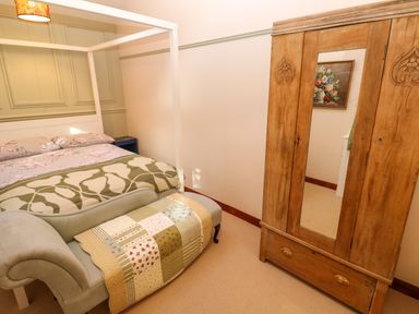 A bedroom with a four-poster bed a wooden wardrobe with a mirror and a chaise lounge at Harveys House in Helston