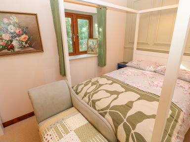 A bedroom with a bed covered with floral and patterned blankets a chair a window with green curtains and framed artwork at Harveys House in Helston