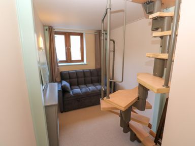 A small room with a dark sofa near a window and a spiral staircase in the corner at Harveys House in Helston