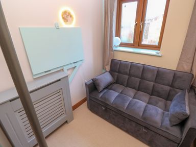 A small room with a gray sofa, two cushions, a window with beige curtains, a blue wall-mounted foldable table, and a gray radiator cover