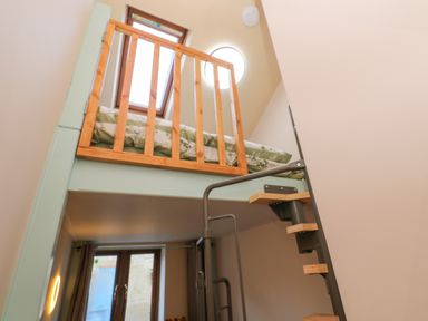 A small loft bed with a wooden railing and metal spiral staircase in a room with windows at Harvey's House in Helston