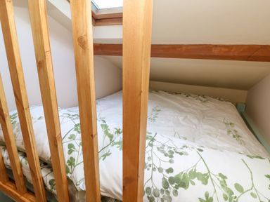 A loft bedroom with a bed with white and green floral bedding behind wooden railings at Harveys House in Helston