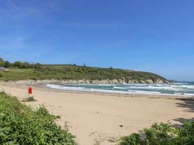 A sandy beach with waves and green hills in the background at Harveys House in Helston