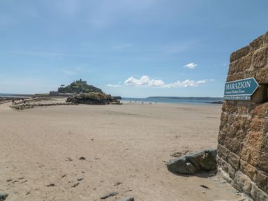 A sandy beach with people walking towards an island with a castle and a sign on a stone wall pointing to Marazion an ancient market town at Harvey's House in Helston