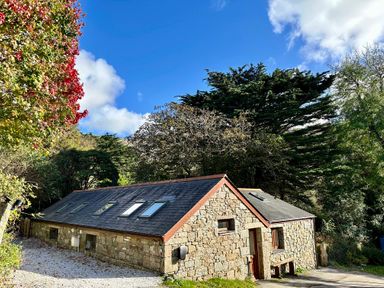 A stone cottage with skylight windows on a slate roof surrounded by trees at Harveys House in Helston