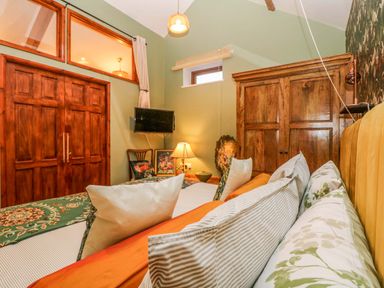 A bedroom with a bed fully lined with pillows a wooden wardrobe a lamp a television and wooden double doors at Harveys House in Helston