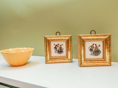 Two small framed vintage art pieces and a yellow scalloped bowl on a white surface against a green wall at Harveys House in Helston