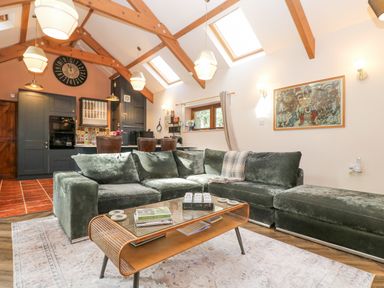 A living room with a green sectional sofa a glass coffee table and an open kitchen with wooden beams on the ceiling at Harveys House in Helston