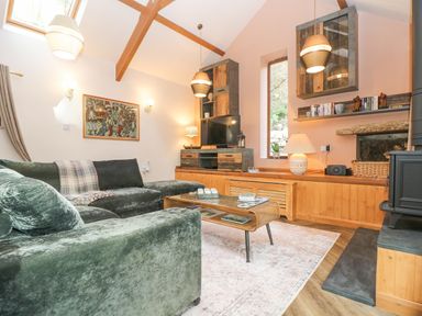A living room with green velvet sofa wooden furniture and a TV at Harveys House in Helston