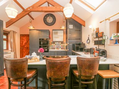 A kitchen with three leather chairs at a marble countertop and wooden beams on the ceiling at Harveys House in Helston