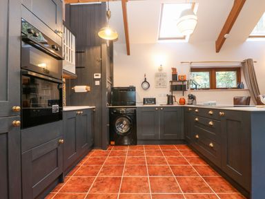 A kitchen with dark cabinets, built-in oven, washing machine, tiled floor and skylights at Harveys House in Helston