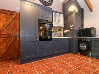 A kitchen with dark cabinets a wooden door a tiled floor a black washing machine a black oven a microwave and patterned tiles on the wall at Harveys House in Helston