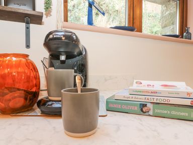 A kitchen counter with a Bosch coffee machine two gray mugs a glass jar and three cookbooks at Harveys House in Helston
