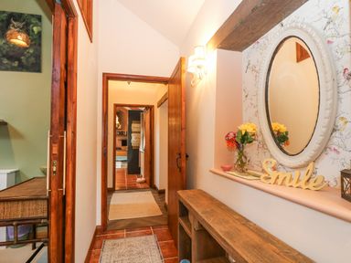 A hallway with a wooden bench and an oval mirror above with flowers in a vase and a sign that says Smile at Harveys House in Helston