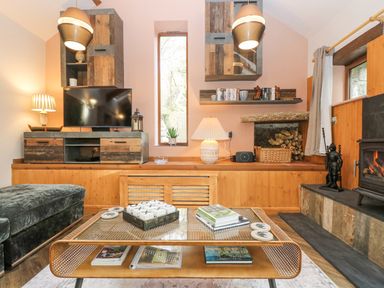 A living room with a glass coffee table books and a tic tac toe set a dark green sofa wooden cabinets a TV and a fireplace with wood at Harveys House in Helston
