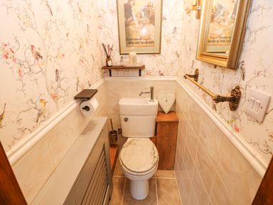 A small bathroom with a toilet a framed picture floral wallpaper and a wall mirror at Harveys House in Helston