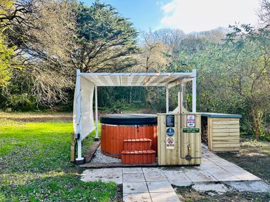 A hot tub with steps under a white canopy in a garden surrounded by trees at Harveys House in Helston