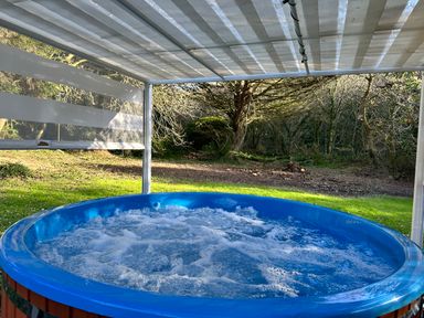 An outdoor hot tub with bubbling water under a striped canopy in a garden with trees at Harvey's House in Helston