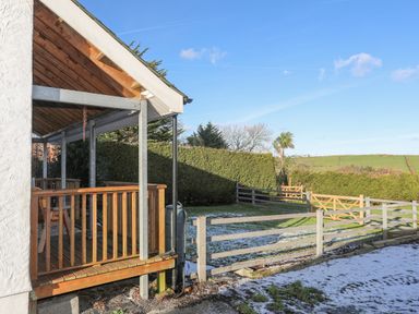 A covered wooden porch with railing overlooking a fenced garden with lawn and hedges at Capel Park (Tyddynod Bach) in Llandyfrydog near Llanerchymedd
