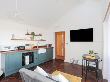 A kitchen area with teal cabinets a wooden countertop a white sink and appliances a dining table with chairs and a wall-mounted TV at Capel Park Tyddynod Bach in Llandyfrydog near Llanerchymedd