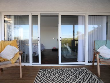 An outdoor deck with two wooden chairs with cushions and blankets and sliding glass doors leading to a bedroom at Capel Park Tyddynod Bach Llandyfrydog near Llanerchymedd