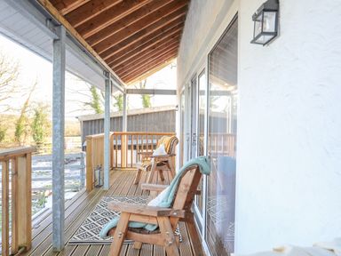 A covered wooden deck with two wooden chairs and a patterned rug at Capel Park Llandyfrydog near Llanerchymedd