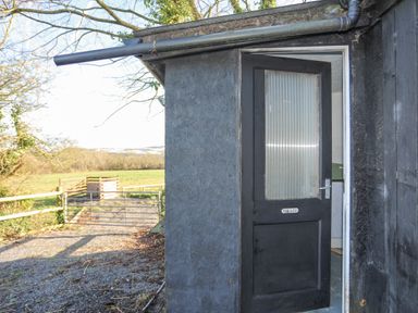 An open black door with a sign reading the loo leading to an outdoor area with a gravel path gate and green fields at Capel Park Tyddynod Bach in Llandyfrydog near Llanerchymedd