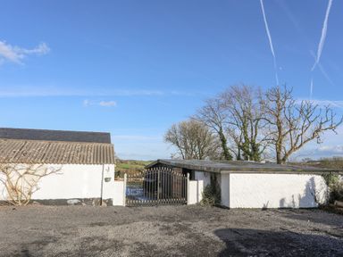 A white building with a corrugated roof and black metal gate next to leafless trees at Capel Park Tyddynod Bach in Llandyfrydog near Llanerchymedd