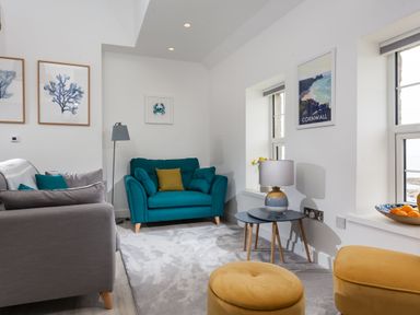 A living room with teal and gray sofas yellow poufs and coastal artwork at Chy Lowen in Porthleven